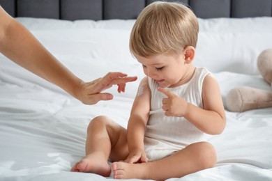 Photo of Mother applying cream onto her baby's arm on bed at home, closeup