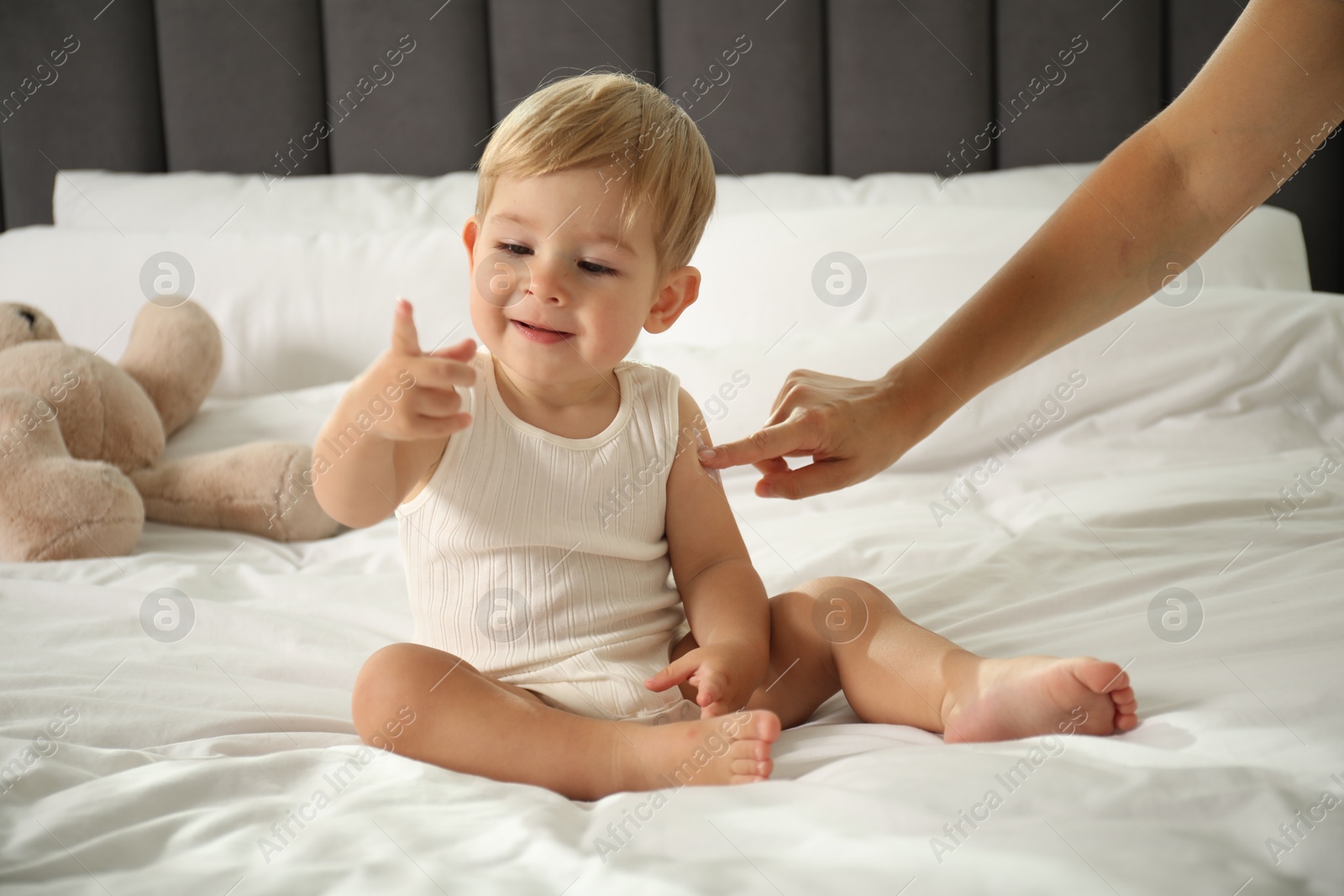 Photo of Mother applying cream onto her baby's arm on bed at home, closeup