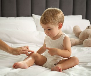 Photo of Mother applying cream onto her baby's body on bed at home, closeup