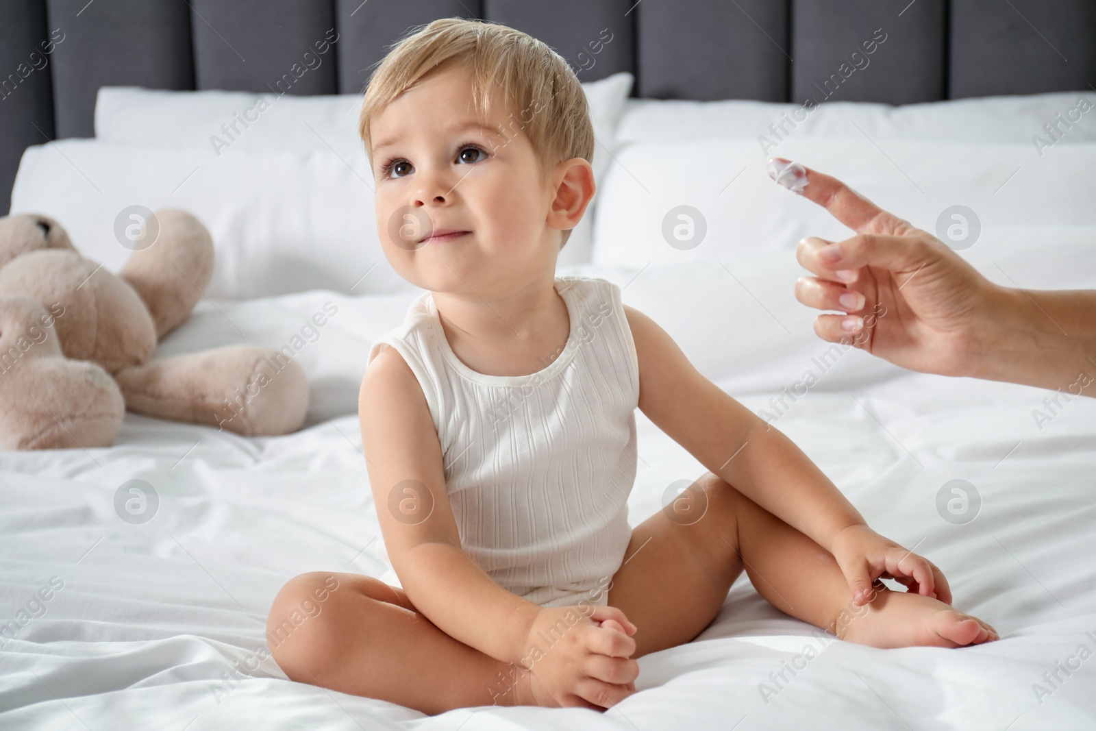 Photo of Mother applying cream onto her baby's body on bed at home, closeup
