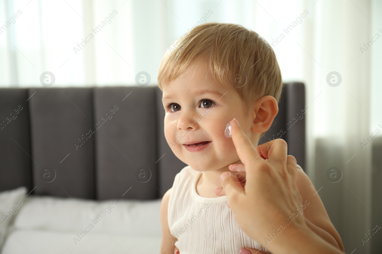 Photo of Mother applying cream onto her baby's face at home, closeup. Space for text