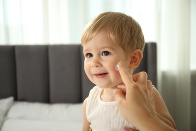 Photo of Mother applying cream onto her baby's face at home, closeup. Space for text