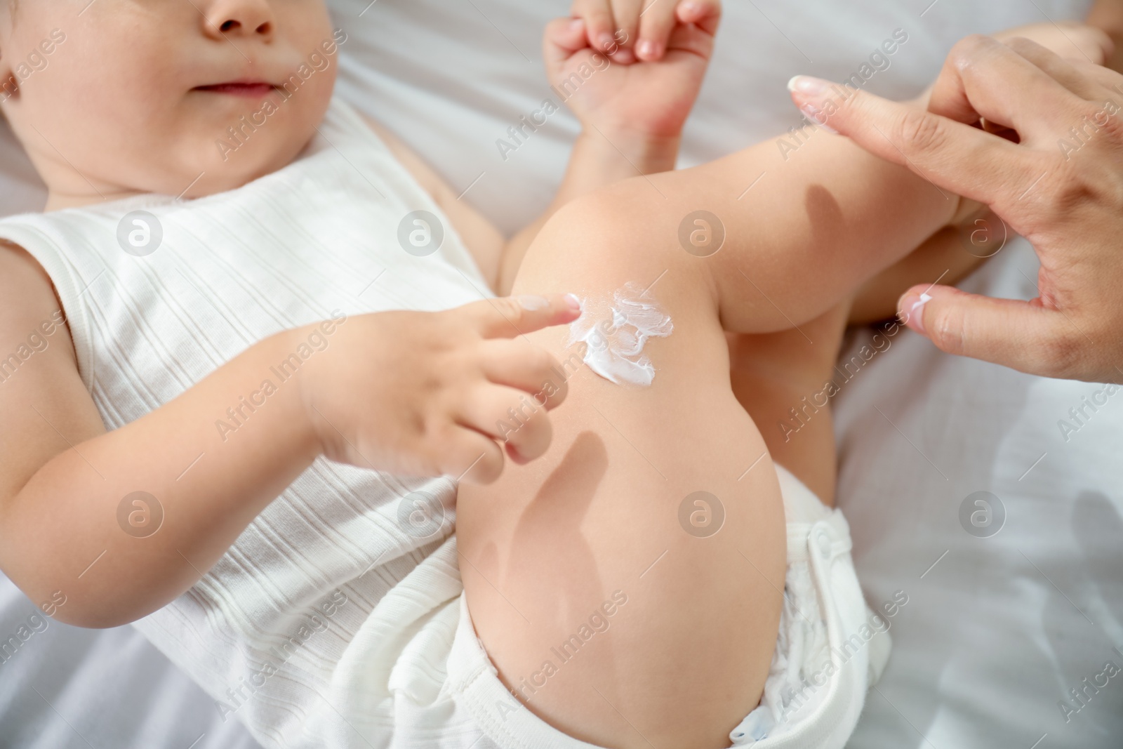 Photo of Mother applying cream onto her baby's leg on bed at home, closeup
