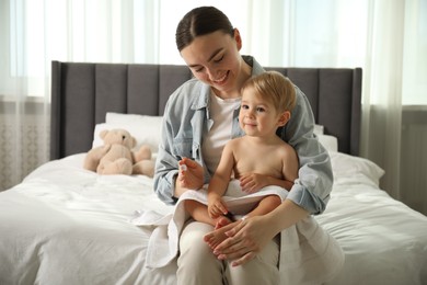 Photo of Mother applying cream onto her baby's leg after bath on bed at home