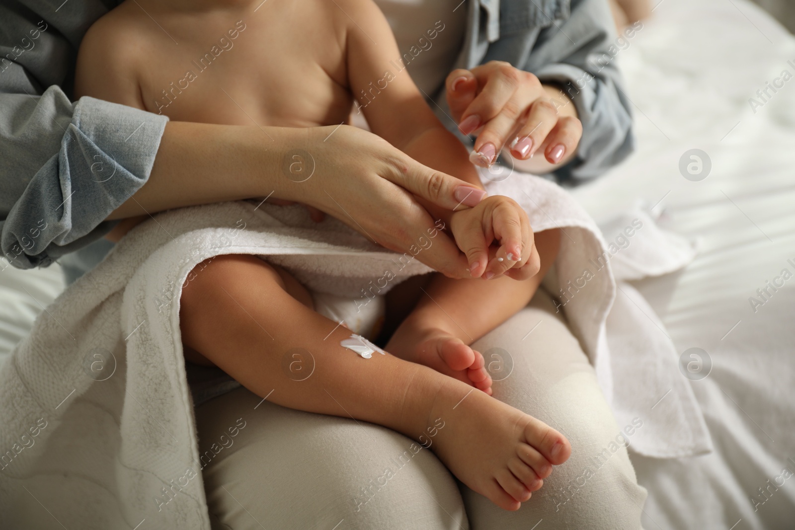 Mother applying cream onto her baby's arm after bath on bed at home, closeup Photo of Mother applying cream onto her baby's arm after bath on bed at home, closeup