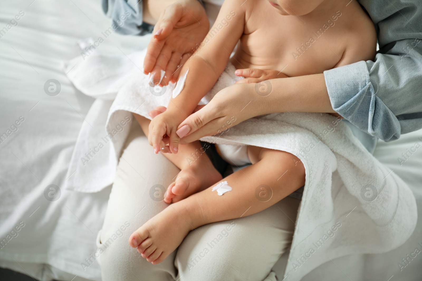 Photo of Mother applying cream onto her baby's arm after bath on bed at home, closeup