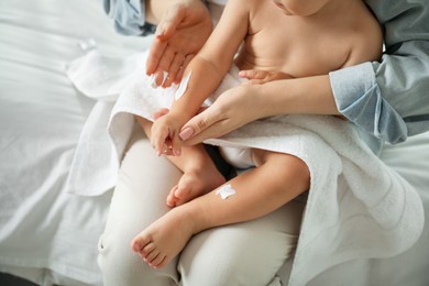 Photo of Mother applying cream onto her baby's arm after bath on bed at home, closeup
