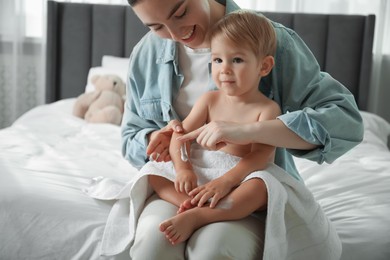 Photo of Mother applying cream onto her baby's arm after bath on bed at home, closeup