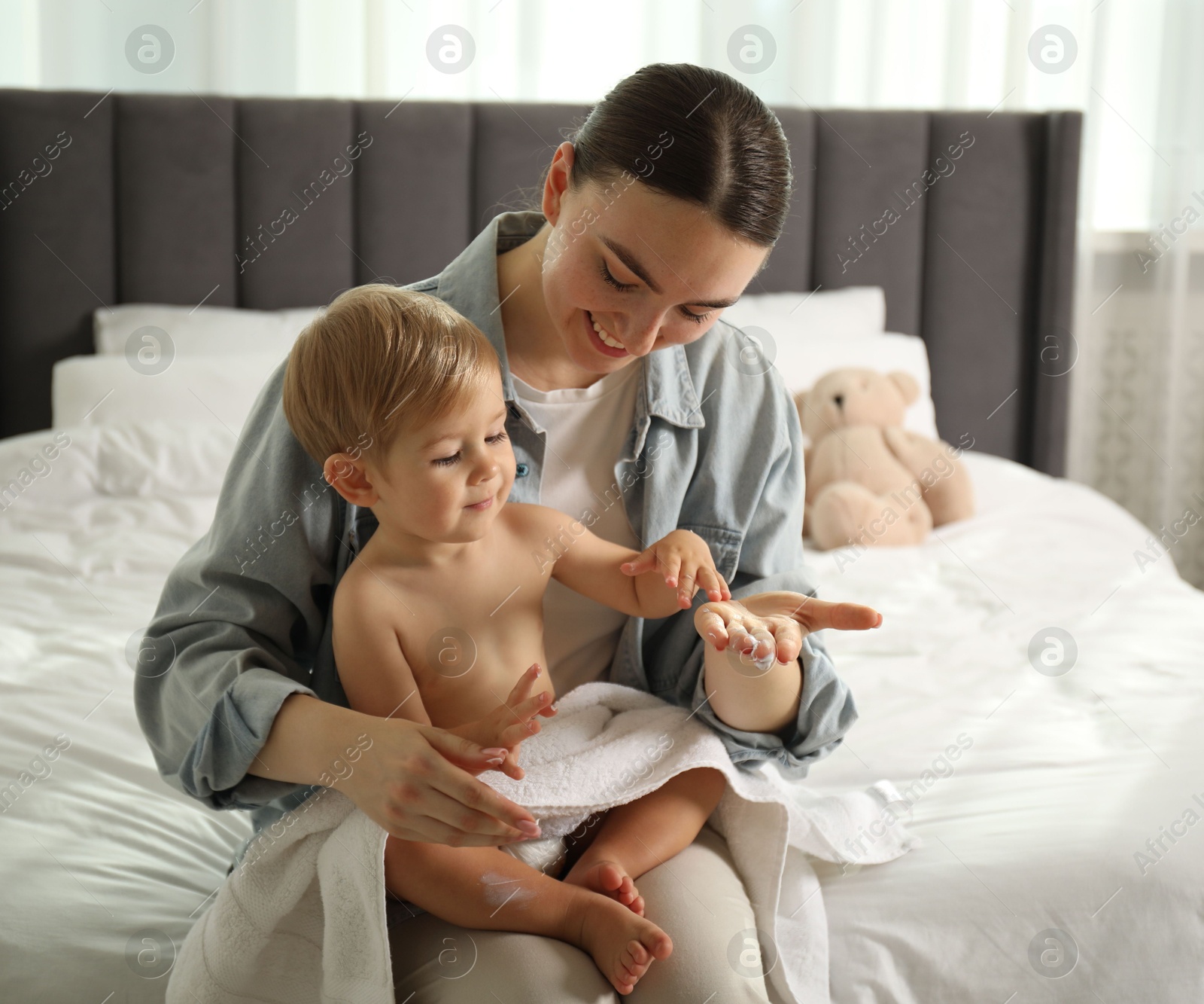 Photo of Mother applying cream onto her baby's body after bath on bed at home