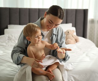 Photo of Mother applying cream onto her baby's body after bath on bed at home