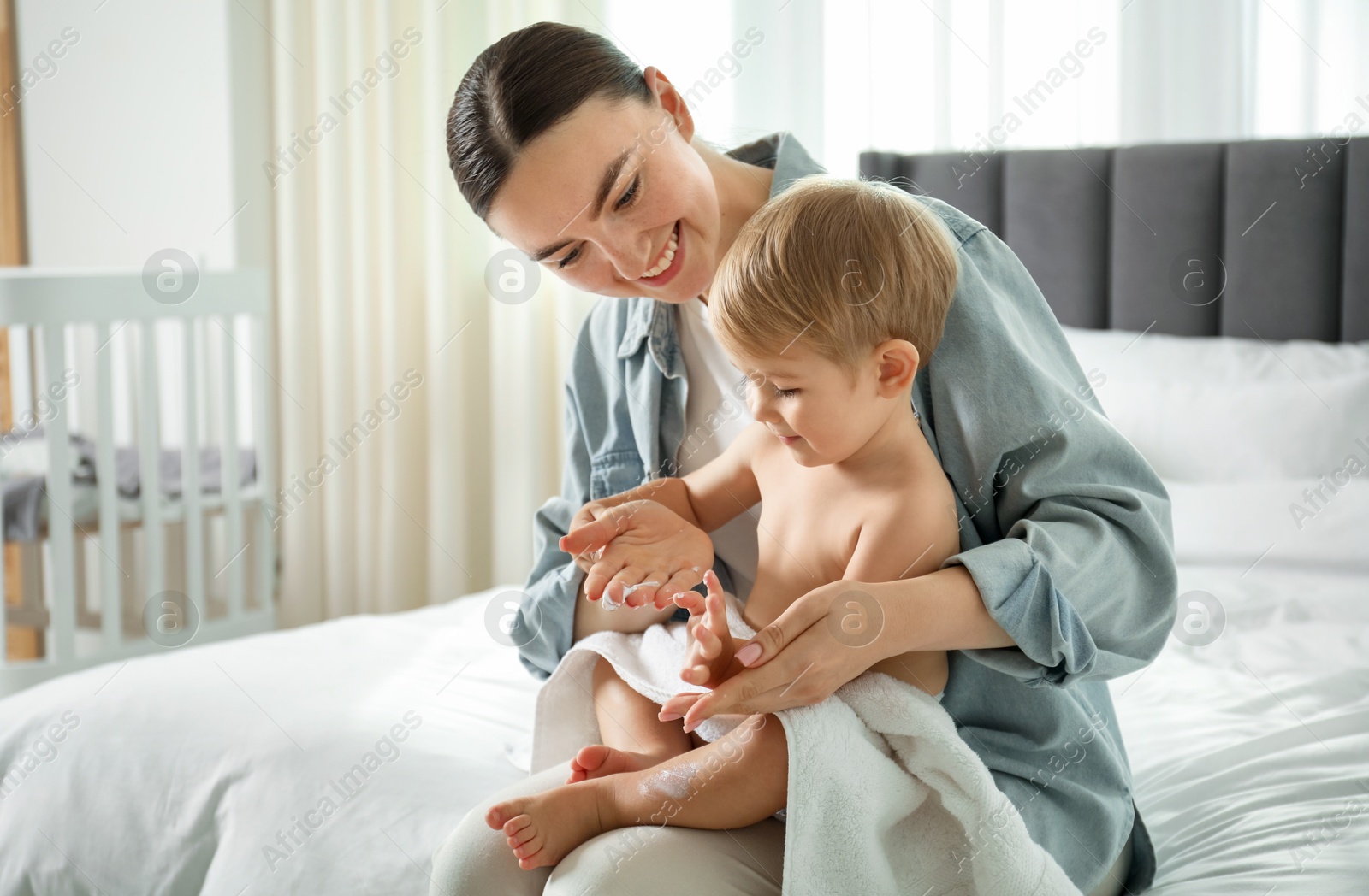 Photo of Mother applying cream onto her baby's body after bath on bed at home
