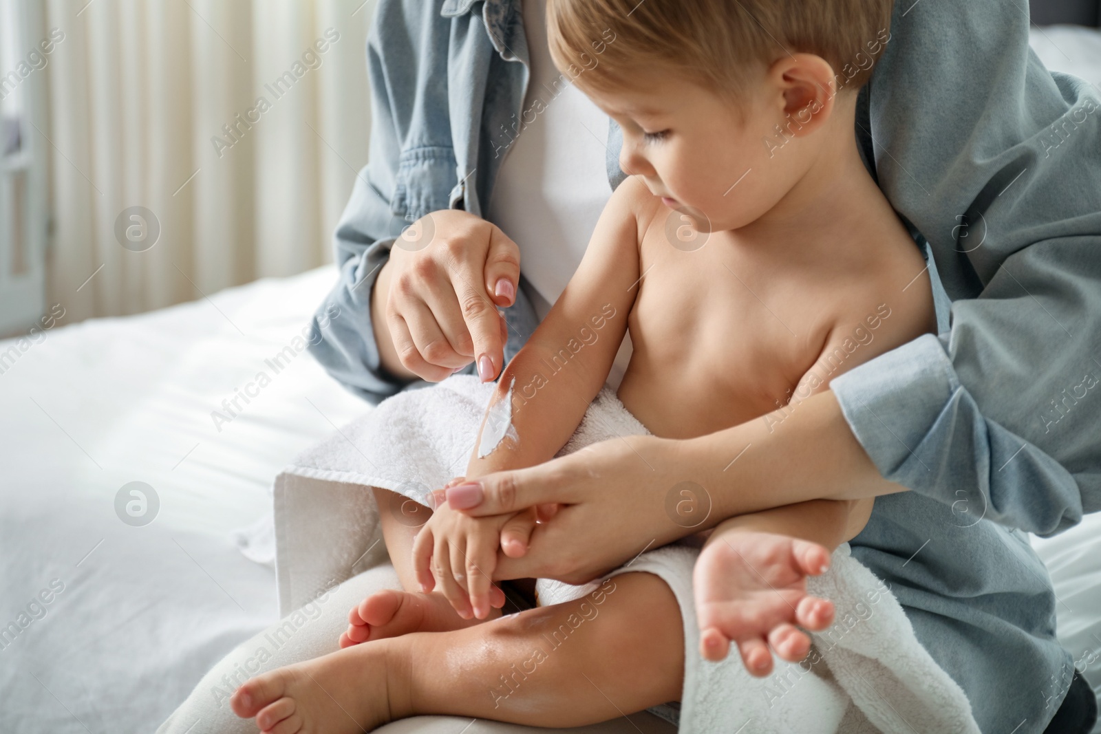 Mother applying cream onto her baby's arm after bath on bed at home, closeup Photo of Mother applying cream onto her baby's arm after bath on bed at home, closeup