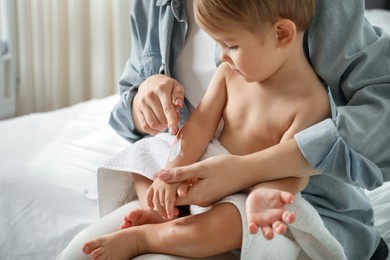 Photo of Mother applying cream onto her baby's arm after bath on bed at home, closeup
