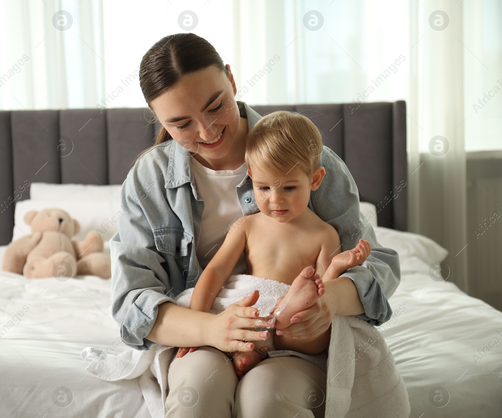 Photo of Mother applying cream onto her baby's foot after bath on bed at home