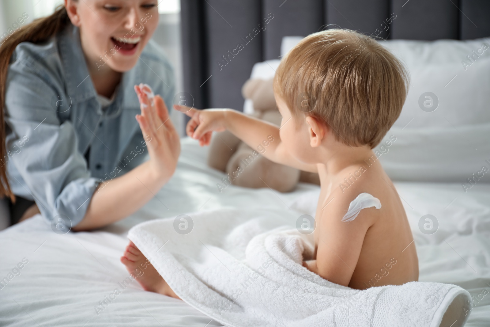 Photo of Mother applying cream onto her baby's body after bath on bed at home, closeup