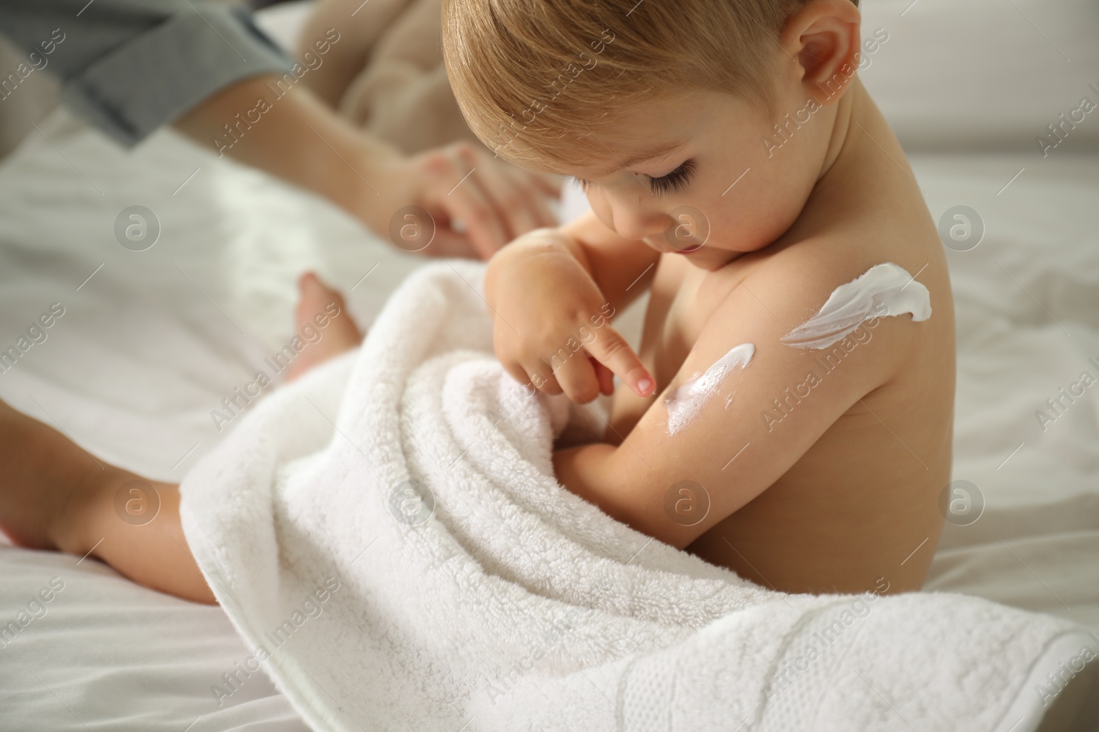 Photo of Mother applying cream onto her baby's body after bath on bed at home, closeup