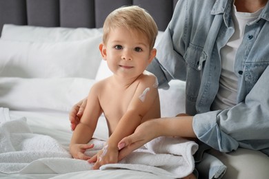 Photo of Mother applying cream onto her baby's body after bath on bed at home, closeup