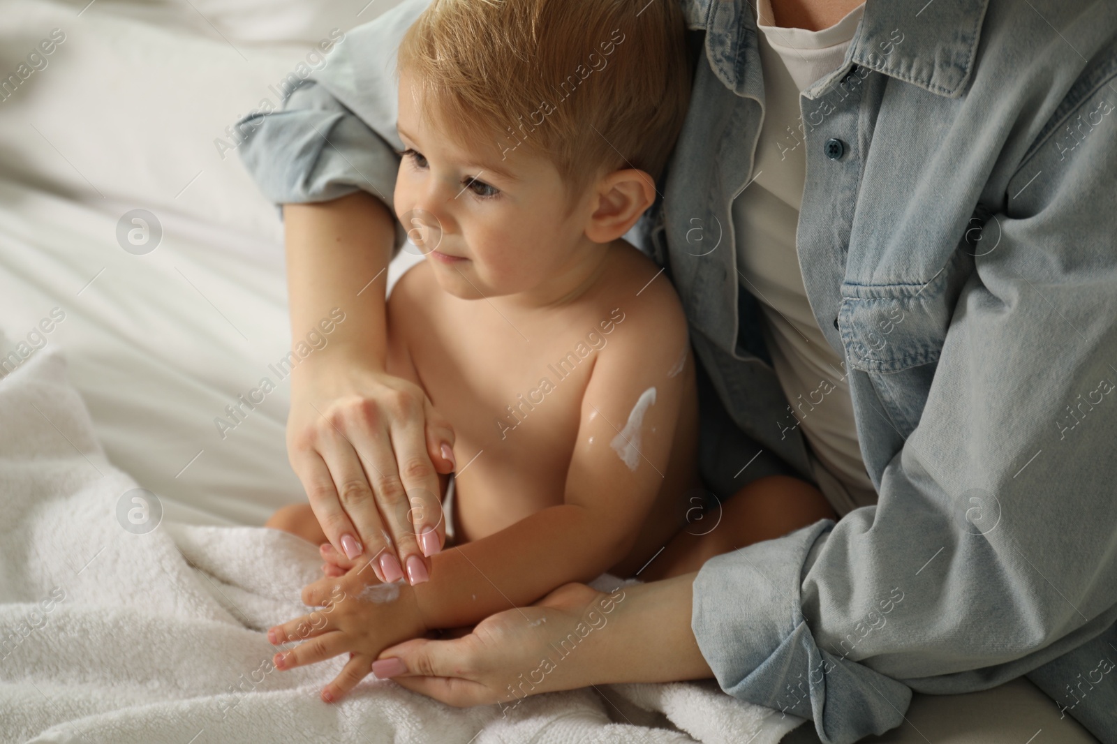 Photo of Mother applying cream onto her baby's body on bed at home, closeup