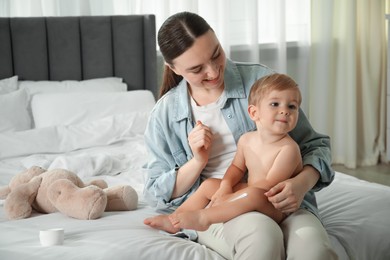 Photo of Mother applying cream onto her baby's leg on bed at home