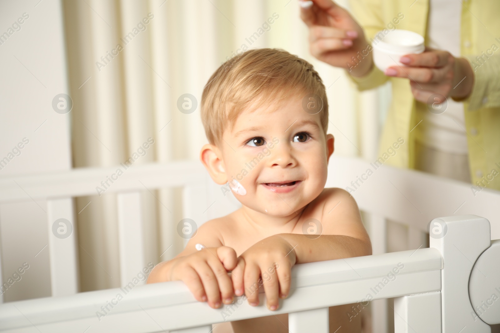 Photo of Cute baby with cream on face in crib and his mom at home