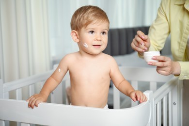 Photo of Mother applying cream onto her baby's body at home, closeup