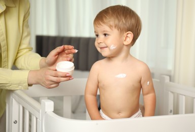 Photo of Mother applying cream onto her baby's body at home, closeup