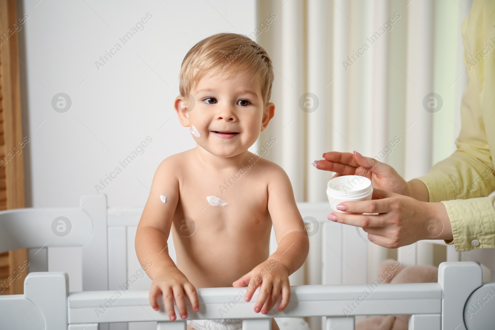 Photo of Mother applying cream onto her baby's body at home, closeup