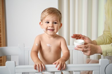 Photo of Mother applying cream onto her baby's body at home, closeup