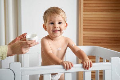 Photo of Mother applying cream onto her baby's body at home, closeup