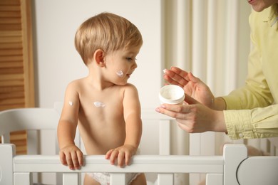 Photo of Mother applying cream onto her baby's body at home, closeup