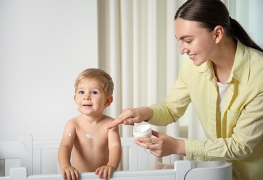 Photo of Mother applying cream onto her baby's body at home