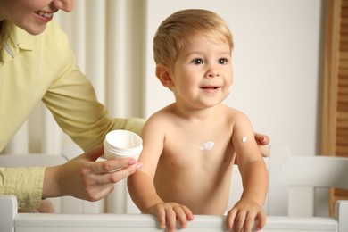 Photo of Mother applying cream onto her baby's body at home, closeup