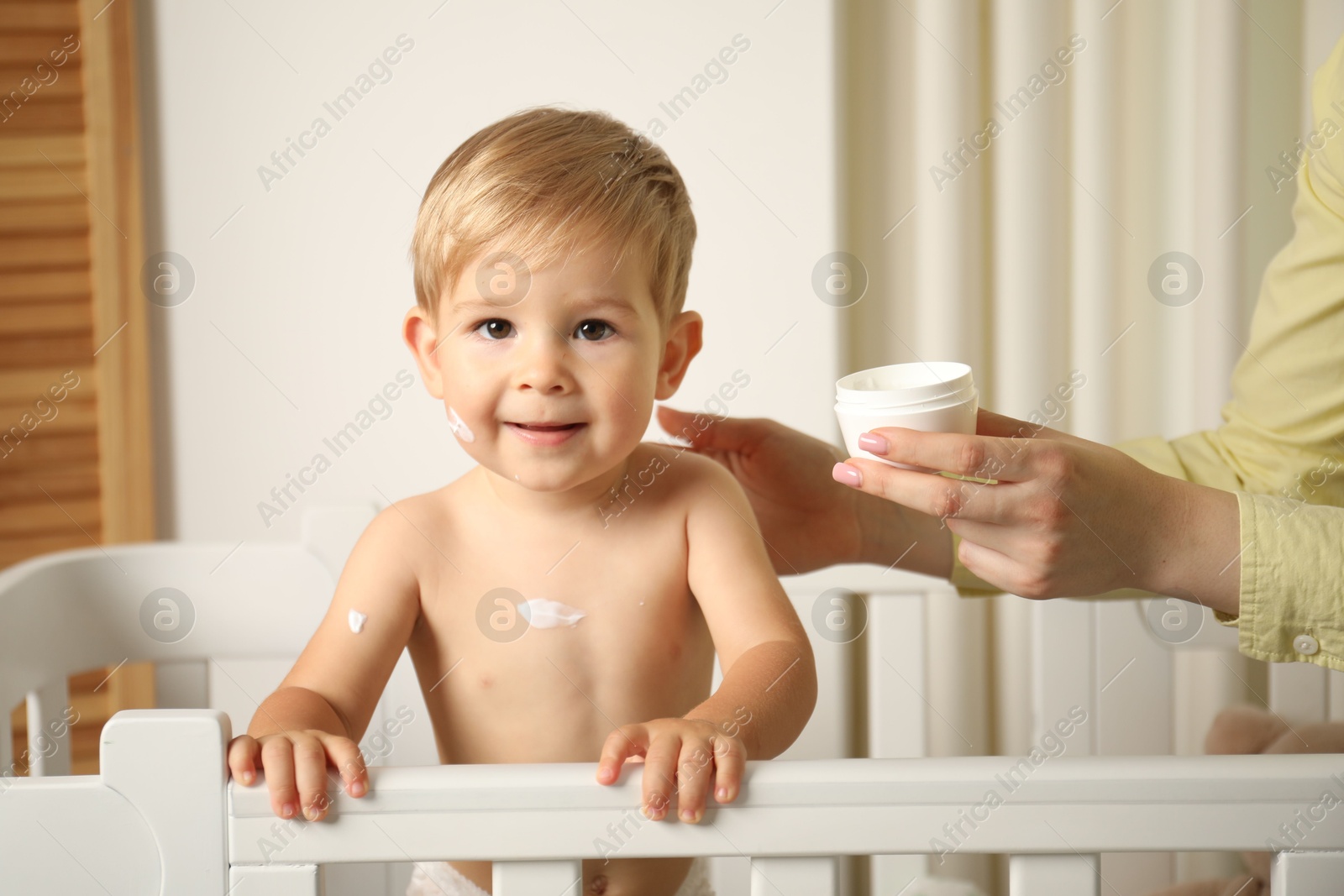 Photo of Mother applying cream onto her baby's body at home, closeup