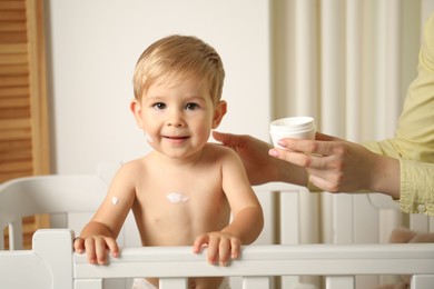 Photo of Mother applying cream onto her baby's body at home, closeup