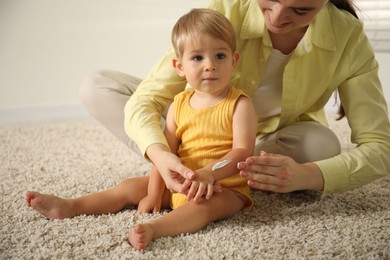 Photo of Mother applying cream onto her baby's arm on floor at home, closeup