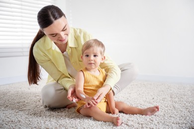 Photo of Mother applying cream onto her baby's arm on floor at home. Space for text