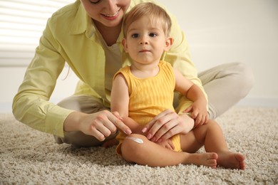 Photo of Mother applying cream onto her baby's leg on floor at home, closeup