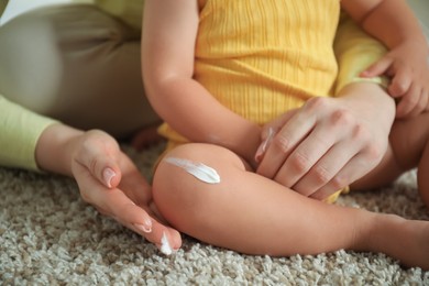 Photo of Mother applying cream onto her baby's leg on floor at home, closeup