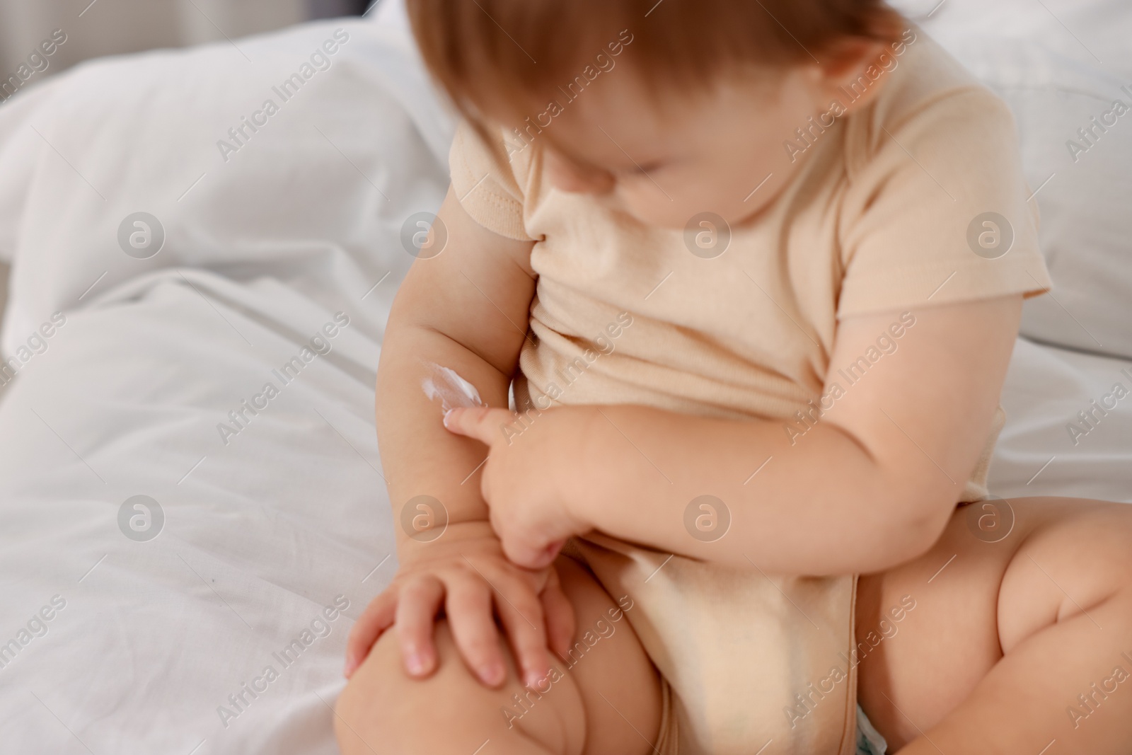 Photo of Cute baby with cream on his arm at home, closeup