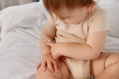 Photo of Cute baby with cream on his arm at home, closeup