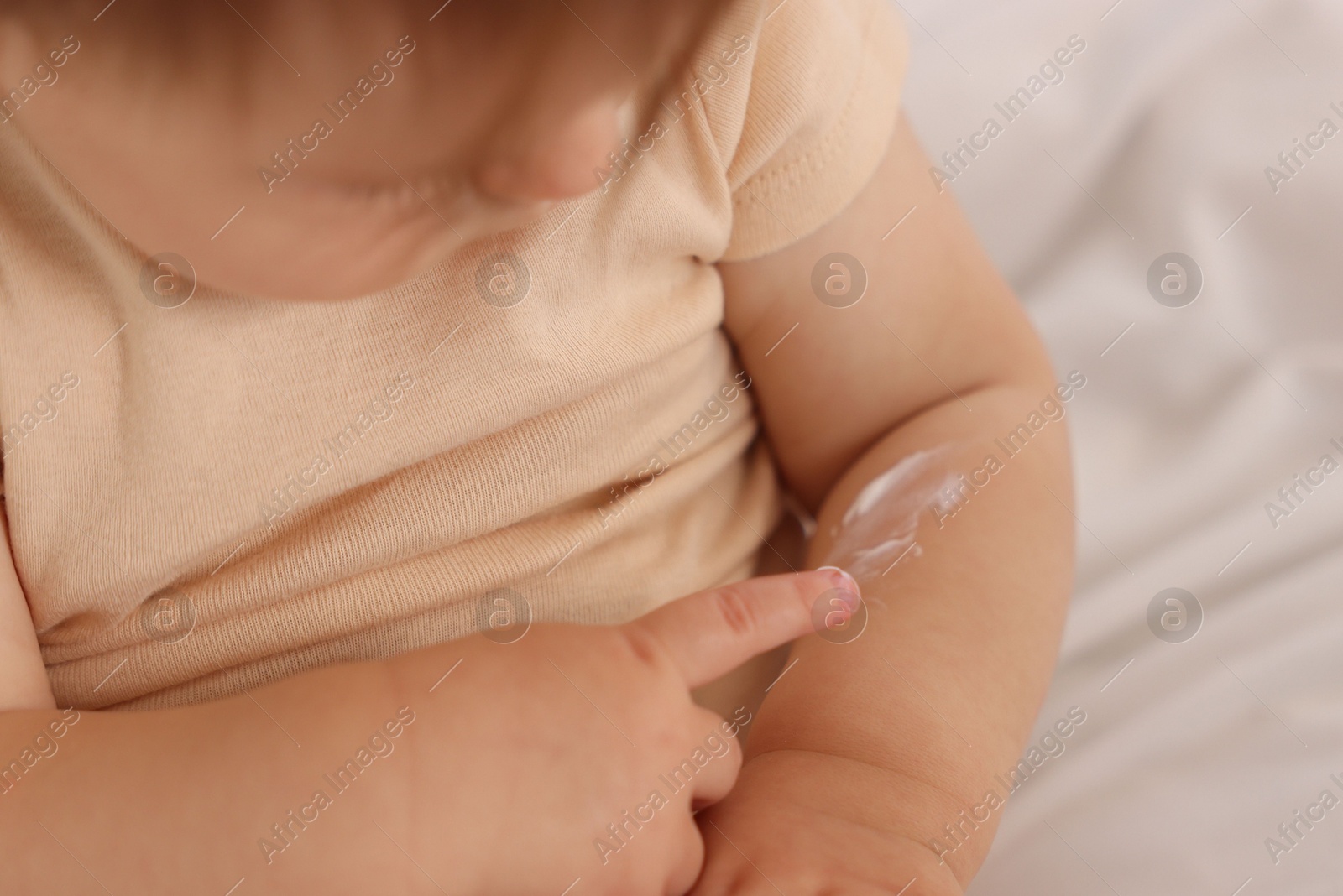 Photo of Cute baby with cream on his arm at home, closeup