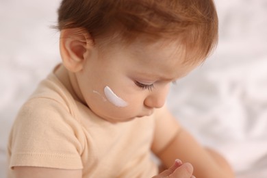 Photo of Cute baby with cream on his face at home, closeup