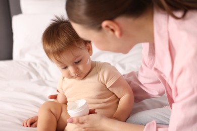Photo of Mother with cream and her baby on bed at home, closeup