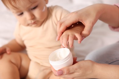 Photo of Mother with cream and her baby on bed at home, closeup