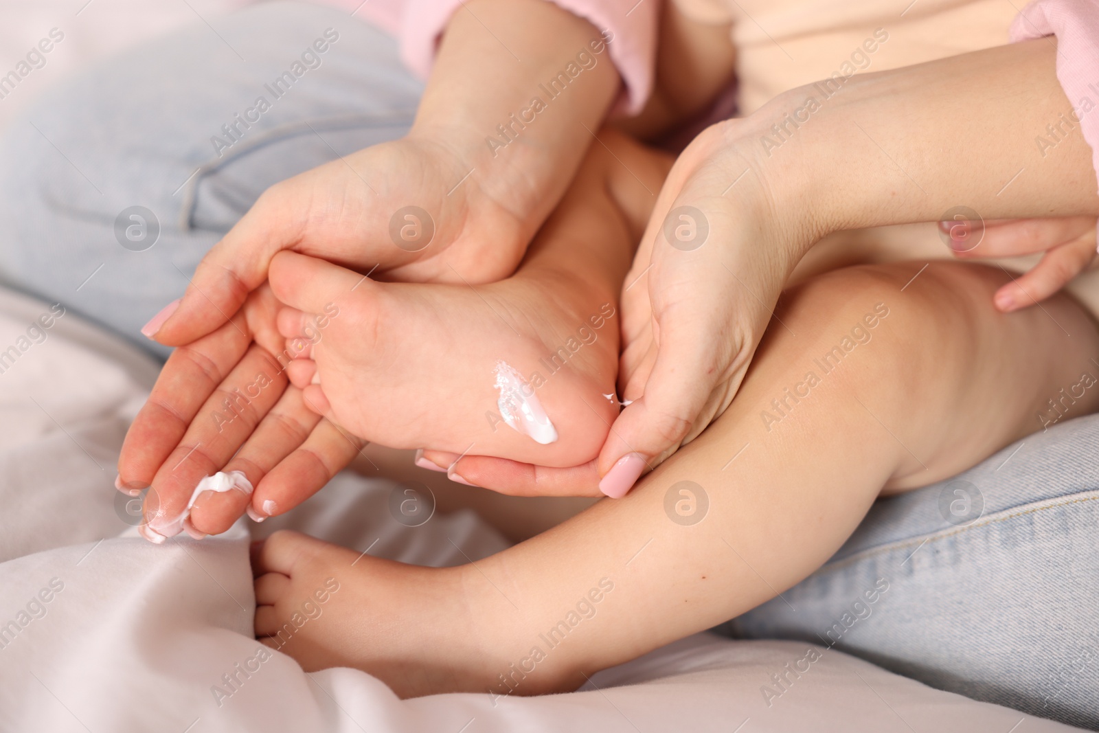 Photo of Mother applying cream onto her baby's foot on bed at home, closeup