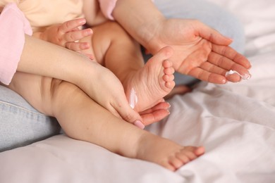 Photo of Mother applying cream onto her baby's foot on bed at home, closeup