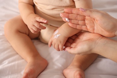 Photo of Mother applying cream onto her baby's arm on bed at home, closeup