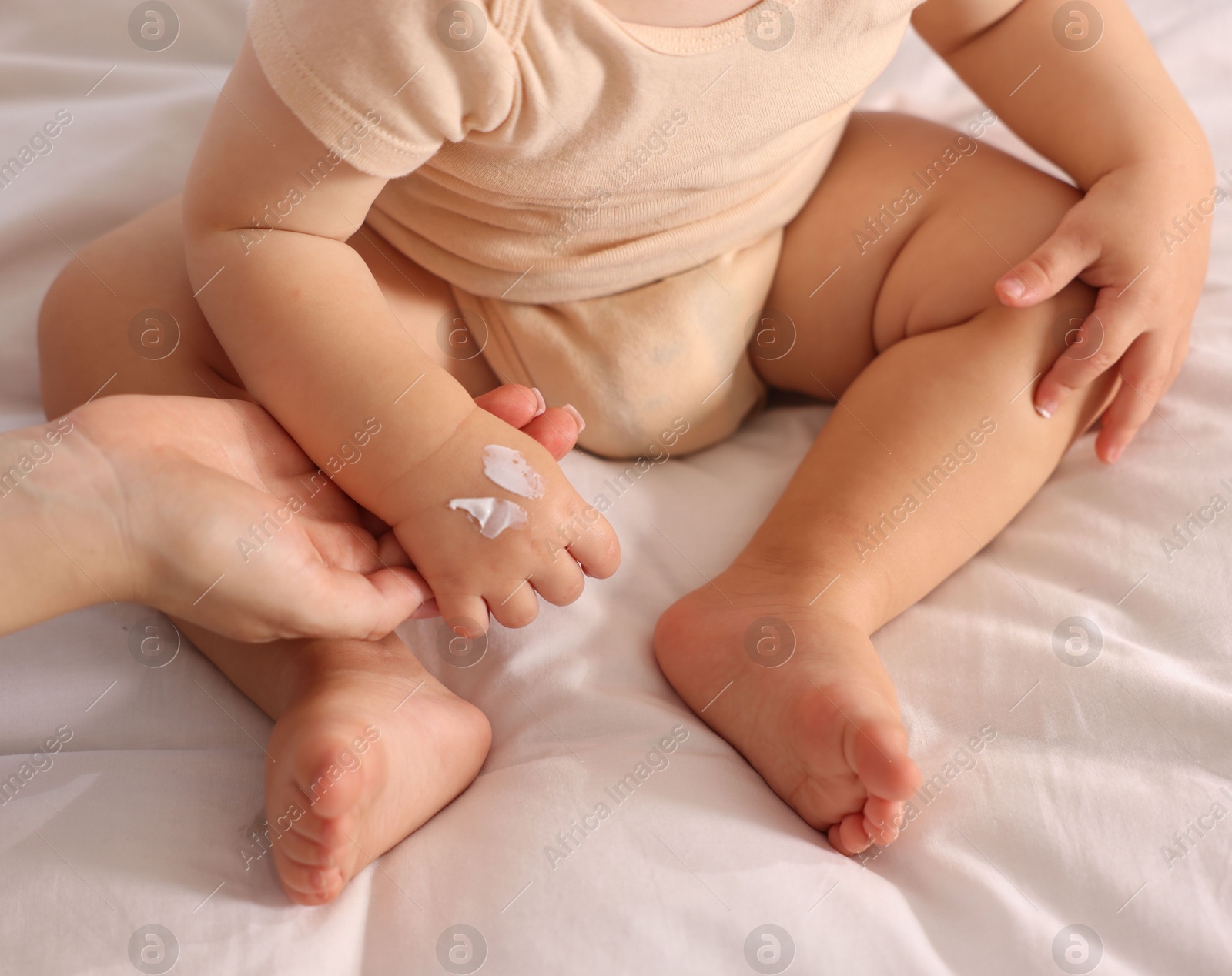 Photo of Mother applying cream onto her baby's arm on bed at home, closeup
