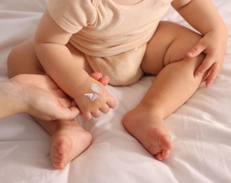 Photo of Mother applying cream onto her baby's arm on bed at home, closeup