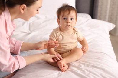 Photo of Mother applying cream onto her baby's body on bed at home